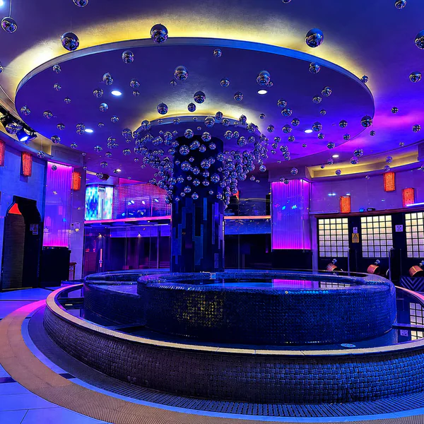 Circular pool under purple-blue lighting and hanging silver spheres